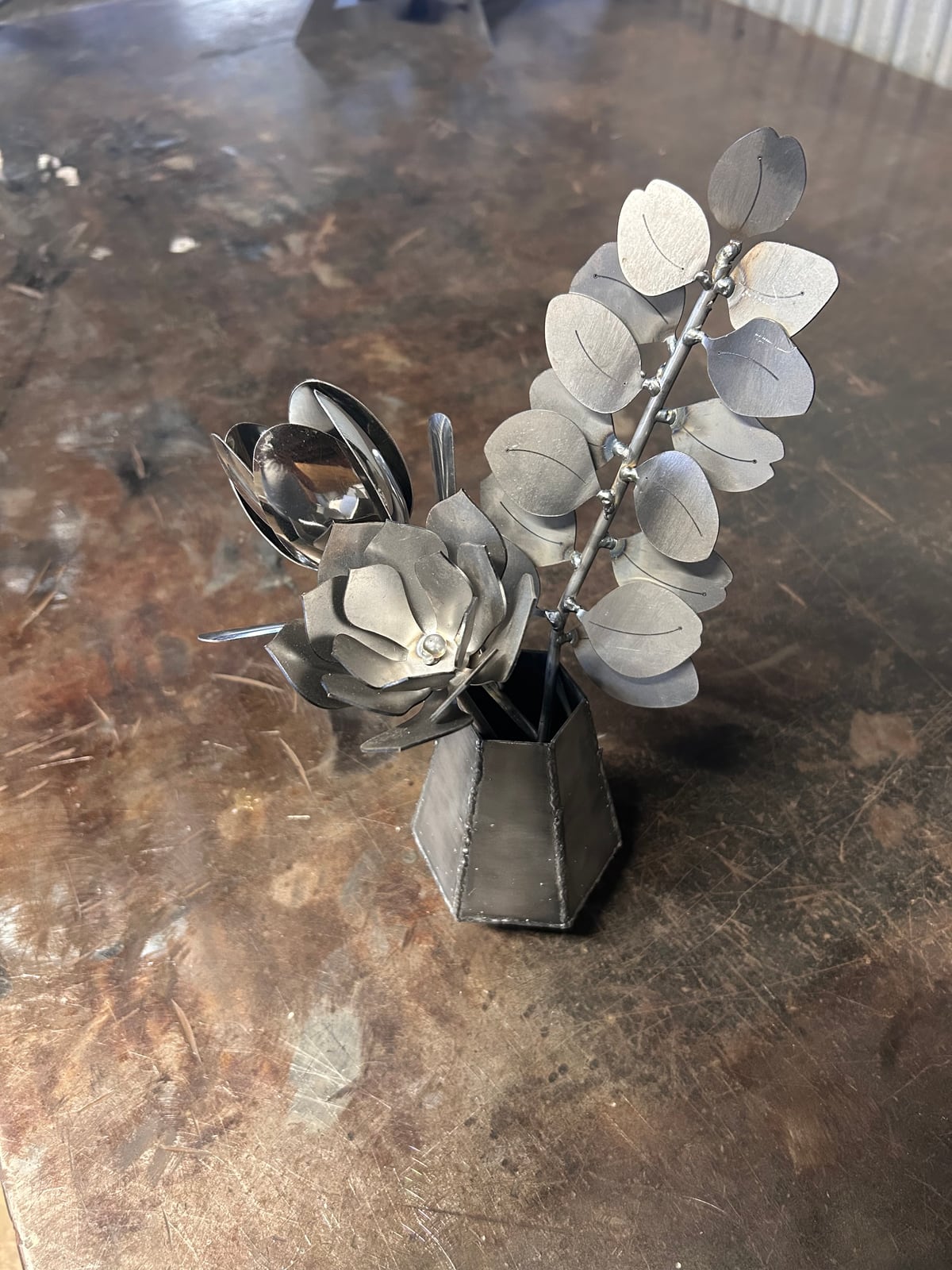 A handmade steel vase holding welded metal flowers and leaves